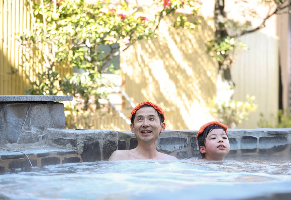 オレンジ色のタオルを頭に置いて温泉に浸かる父親と息子